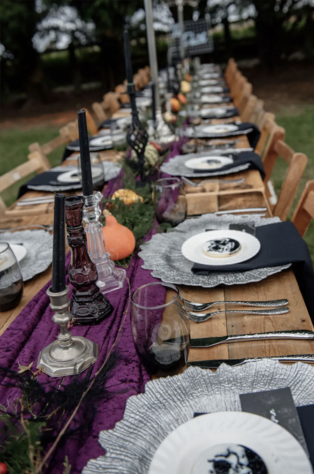 Halloween wedding table with a purple runner, deep purple and silver cutlery, placemats and candleholders